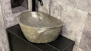 A bathroom with a black cabinet, a stone sink, and a textured wall.