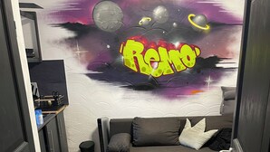 A room with a sofa, a wall with a space-themed mural, and a door leading to another room.
