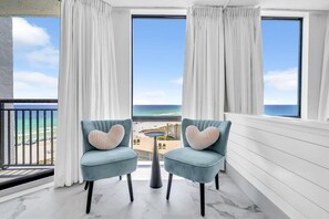 Un balcon avec deux chaises, une petite table et une vue sur la plage et l’océan.
