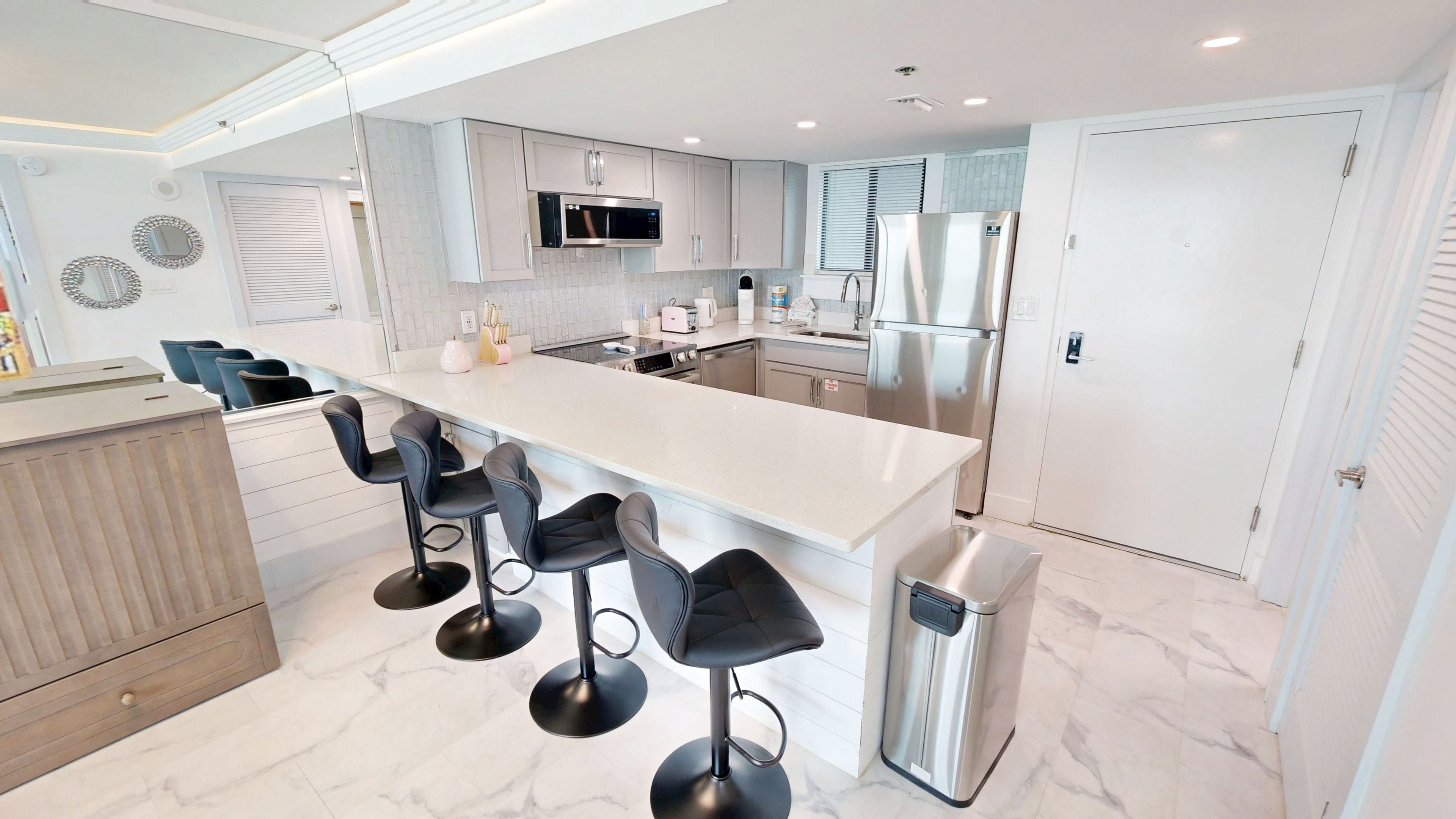 Una cocina moderna con una isla central, taburetes de bar, electrodomésticos de acero inoxidable y un salpicadero de azulejos.