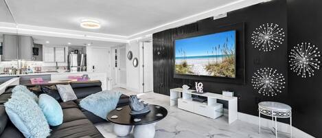 Un salon moderne avec un canapé en cuir noir, une table basse et un grand téléviseur à écran plat fixé au mur.