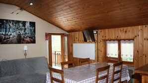 A wooden cabin interior with a dining table, chairs, a sofa, and a painting of deer. - Soffio di Miele, the perfect place to visit Valtournenche (Pâquier)