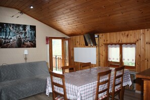 A wooden cabin interior with a dining table, chairs, a sofa, and a painting of deer. - Soffio di Miele, the perfect place to visit Valtournenche (Pâquier)