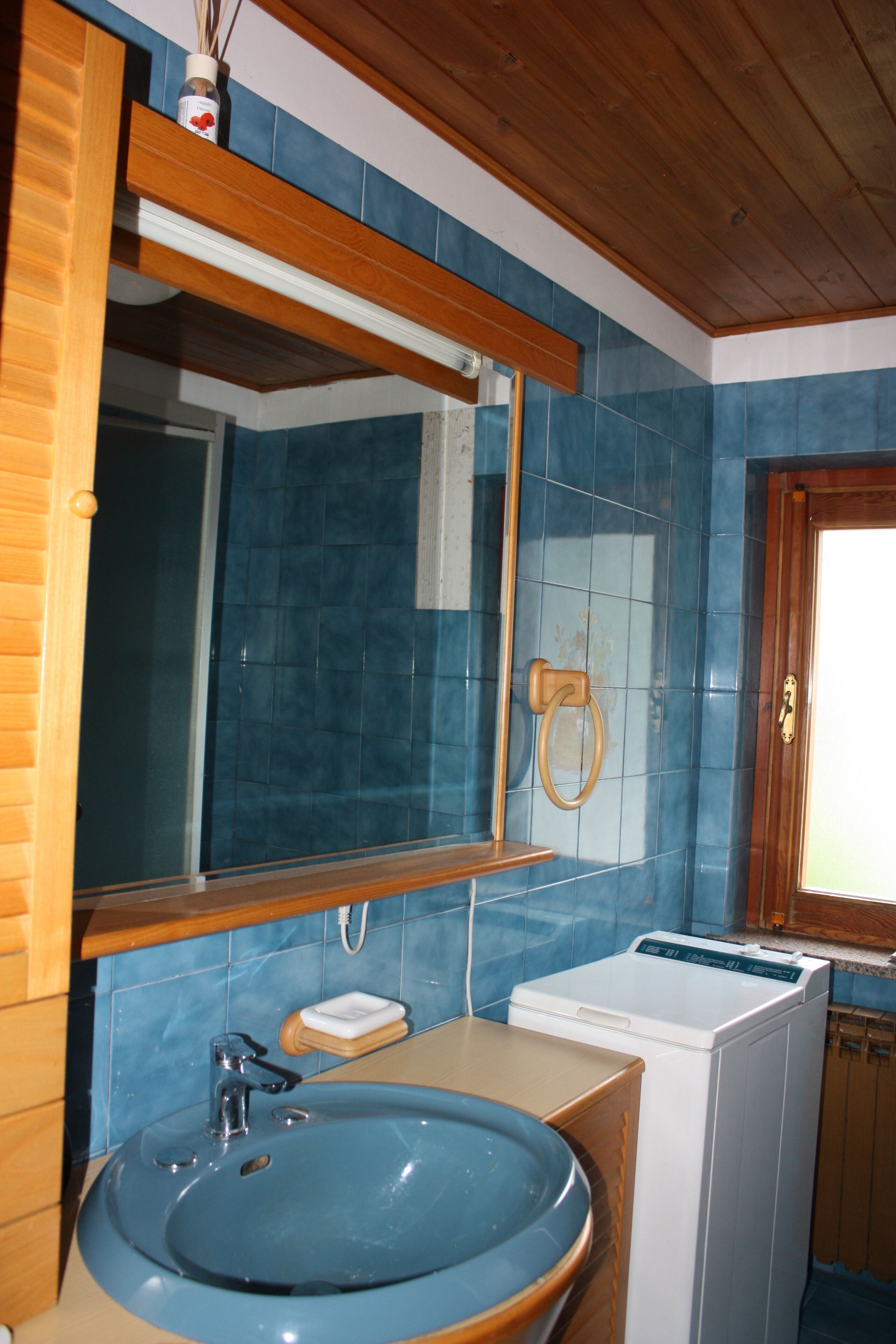 A bathroom with a blue sink, wooden vanity, a mirror, a towel ring, and a washing machine.
