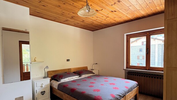 A bedroom with a wooden ceiling, a bed with a heart-shaped nightstand, a window with a view, and a radiator. - Soffio di Miele, the perfect place to visit Valtournenche (Pâquier)