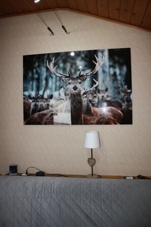 A bedroom with a large deer antler painting on the wall, a bedside lamp, and a quilted bedspread. - Soffio di Miele, the perfect place to visit Valtournenche (Pâquier)