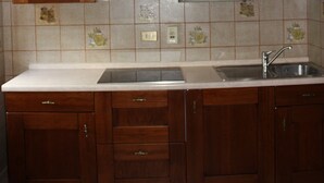 A kitchen with wooden cabinets, a tiled backsplash, and a stainless steel sink. - Soffio di Miele, the perfect place to visit Valtournenche (Pâquier)