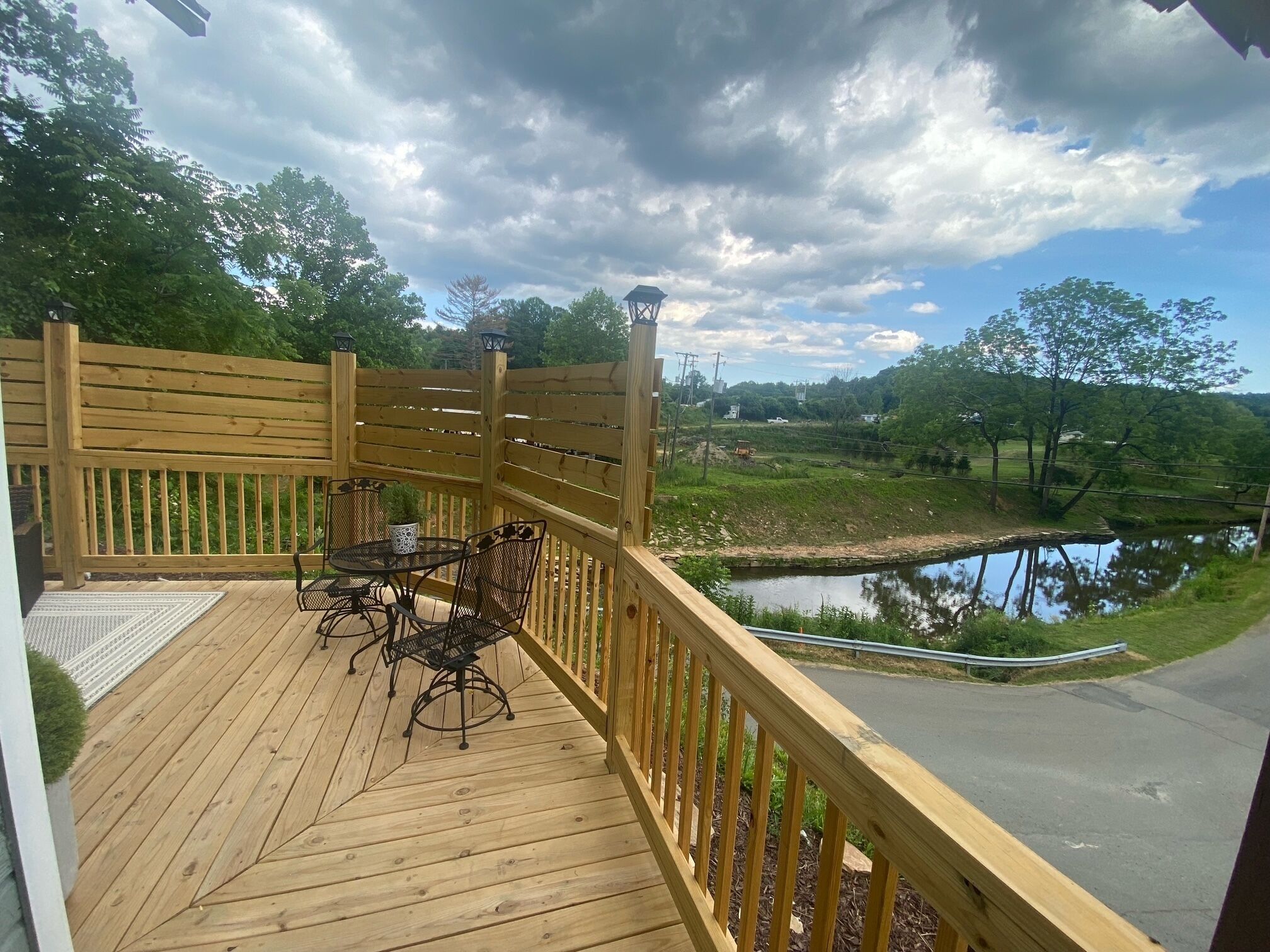 Une terrasse en bois avec une table et des chaises, donnant sur une étendue d’eau et une zone verdoyante.