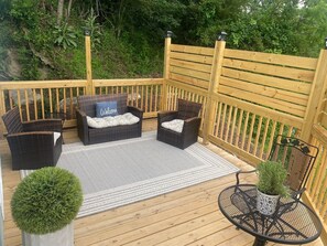 Eine Terrassenausstattung mit Holzlattenzaun, Korbmöbeln, einem Willkommenskissen, einem gemusterten Teppich und einem Blumentopf.