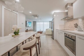 A modern kitchen with a dining area, white cabinetry, and a large window. - Luxury 3 BD Condo, 5 min Walk to Palm Beach Zone! (Noord)