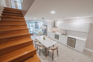 A modern kitchen with white cabinetry, a dining area with a white table and chairs, and a wooden staircase. - Luxury 3 BD Condo, 5 min Walk to Palm Beach Zone! (Noord)