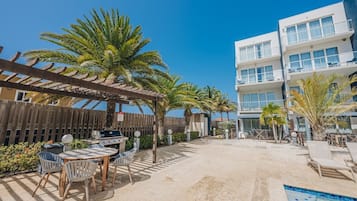 A poolside area with a barbecue setup, outdoor seating, and a building with balconies.