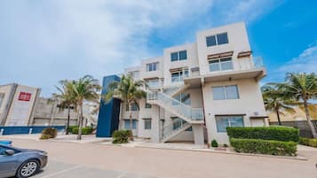 A multi-story residential building with a central staircase, balconies, and palm trees.