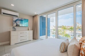 Une chambre dotée d’un grand lit, d’une commode, d’un climatiseur et offrant une vue sur une piscine et des immeubles.