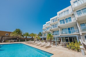 A hotel with a swimming pool, outdoor seating, and palm trees. - Luxury 3 BD Condo, 5 min Walk to Palm Beach Zone! (Noord)