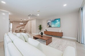 A modern living room with a sofa set, a coffee table, a TV, and a dining area in the background. - Luxury 3 BD Condo, 5 min Walk to Palm Beach Zone! (Noord)