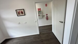 A hallway with a fire alarm panel, a fire extinguisher, and a framed picture on the wall. - 2024Built/AC & Bath each Room/Study/TownCentre/SDA (Werribee)