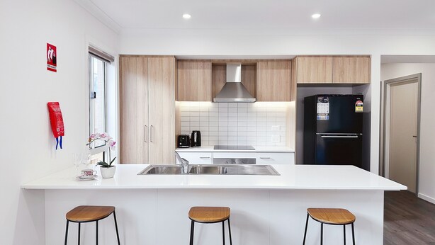 A modern kitchen with a central island, wooden cabinets, a black refrigerator, and a window with a fire blanket sign. - 2024Built/AC & Bath each Room/Study/TownCentre/SDA (Werribee)
