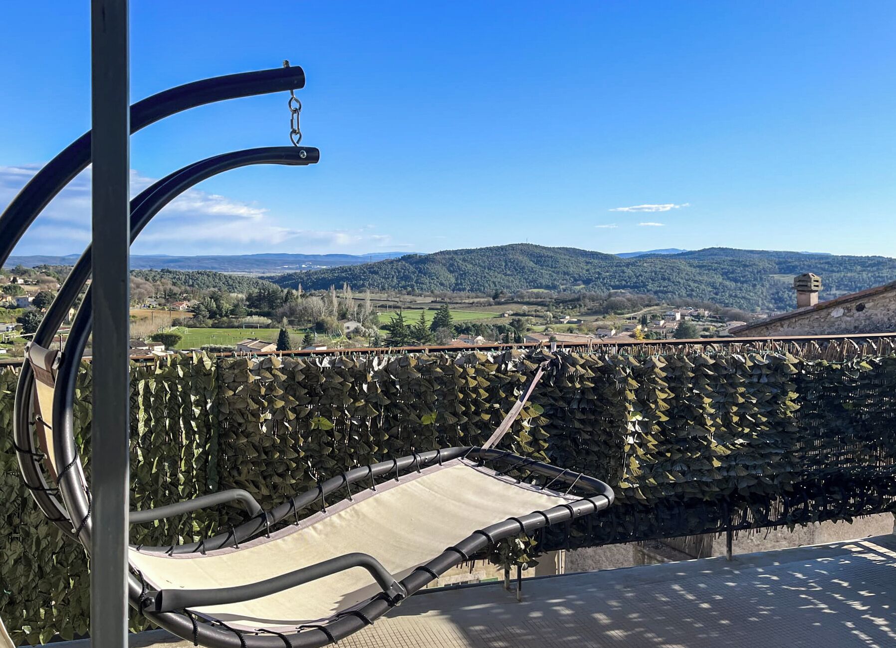 A hammock chair on a balcony overlooking a vineyard.