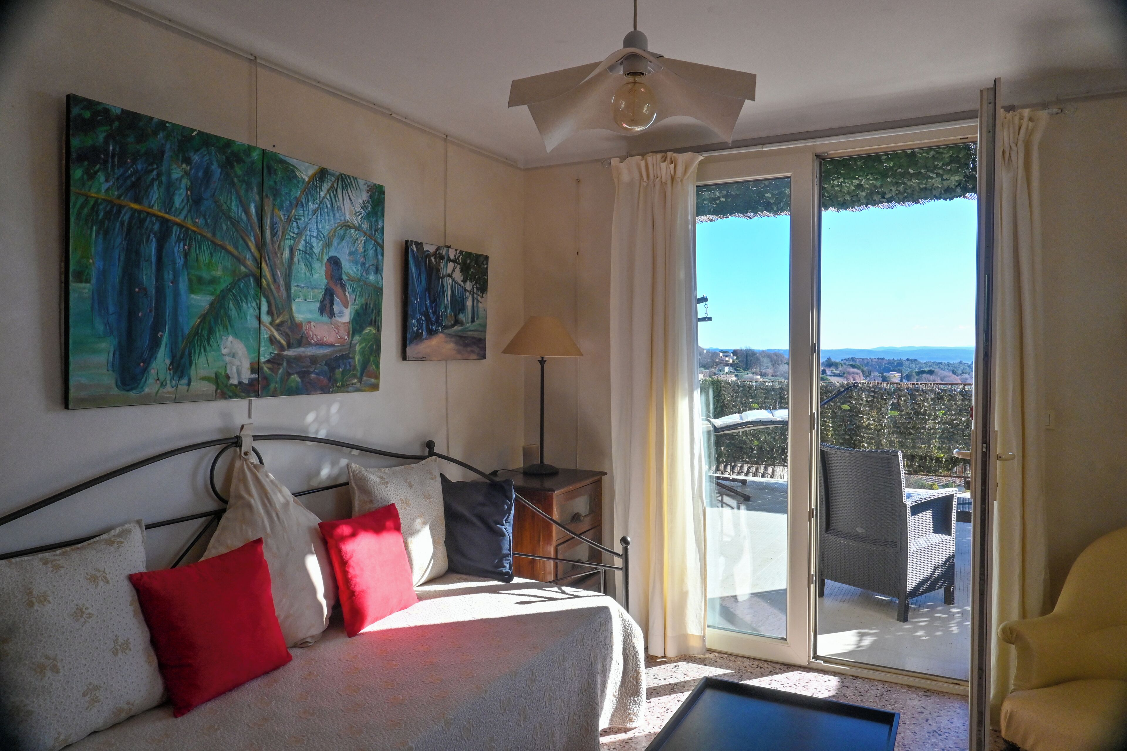Een slaapkamer met een bed, een bank, een schilderij, een lamp en uitzicht door een schuifdeur.