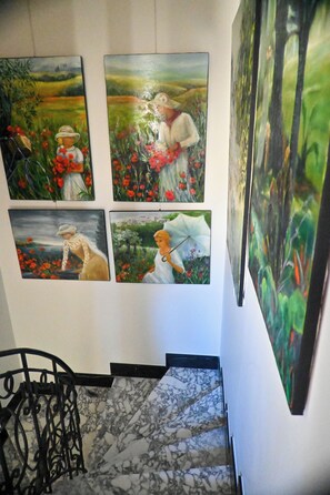 Eine Marmortreppe führt zu einer Zwischenebene, wo vier Gemälde an der Wand ausgestellt sind.