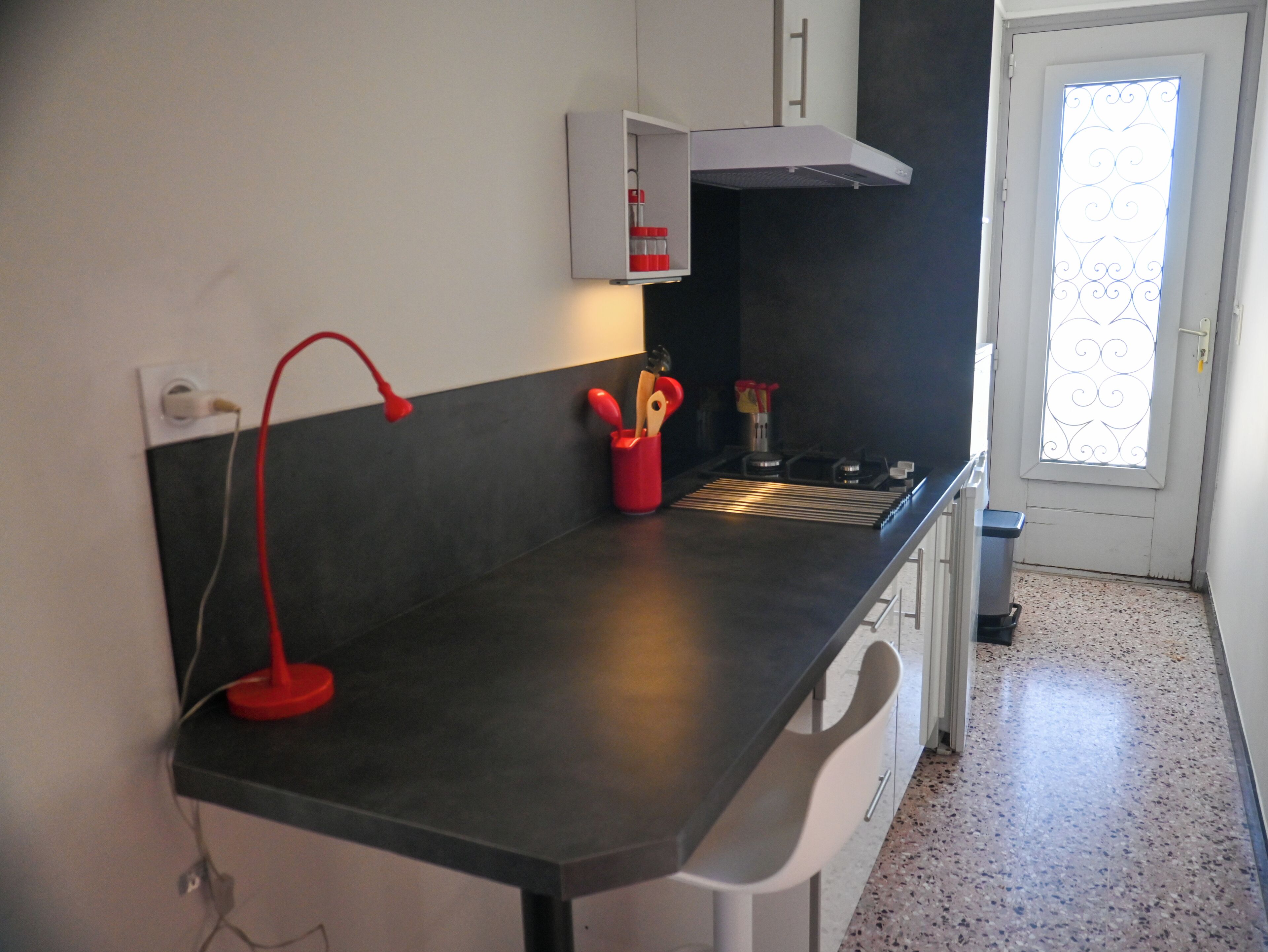 A kitchen with a black countertop, a red lamp, and a window with decorative iron bars.