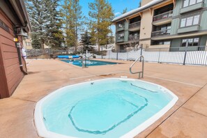 Un espace piscine comprenant un jacuzzi, une petite piscine et une terrasse entourée d’une clôture.