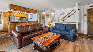 A living room with a brown leather sofa, a blue sofa, a wooden coffee table, a kitchen area with a refrigerator and microwave, and a wall with skis. - Phoenix 219 – Your Gondola-Side Mountain Retreat in Steamboat Springs! (Steamboat Springs)