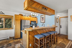 Une cuisine avec des meubles en bois, un réfrigérateur en acier inoxydable, un four à micro-ondes et un îlot central en bois doté de tabourets de bar.