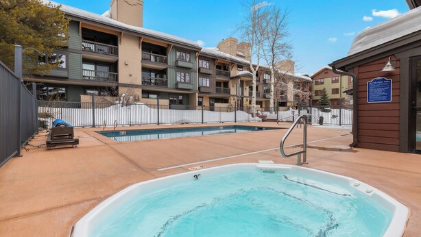 A swimming pool area with a hot tub, a covered seating area, and a fenced patio. - Phoenix 219 – Your Gondola-Side Mountain Retreat in Steamboat Springs! (Steamboat Springs)