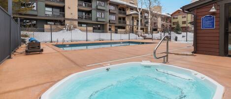 A swimming pool area with a hot tub, a covered seating area, and a fenced patio.