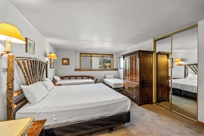 A hotel room with a large bed, two smaller beds, a wardrobe, a mirror, and a window with a view. - Cozy 2BR Ski Condo | Gas Fireplace & Shuttle (Steamboat Springs)