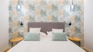 A bed with a headboard, two bedside tables, and a wall with a leaf pattern. - Apartment in Las Palmas Near Playa Alcaravaneras (Las Palmas de Gran Canaria)