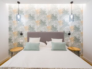 A bed with a headboard, two bedside tables, and a wall with a leaf pattern. - Apartment in Las Palmas Near Playa Alcaravaneras (Las Palmas de Gran Canaria)