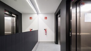 A modern elevator lobby with two elevators, fire extinguishers on the wall, and a clean, tiled floor. - Apartment in Las Palmas Near Playa Alcaravaneras (Las Palmas de Gran Canaria)
