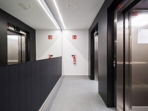 A modern elevator lobby with two elevators, fire extinguishers on the wall, and a clean, tiled floor. - Apartment in Las Palmas Near Playa Alcaravaneras (Las Palmas de Gran Canaria)
