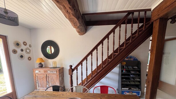 Ein Holztisch mit einer gewebten Tischmatte, einer Metallschüssel und einem Holzschrank mit einer Lampe. Eine Treppe mit Holzgeländern führt auf eine erhöhte Ebene.