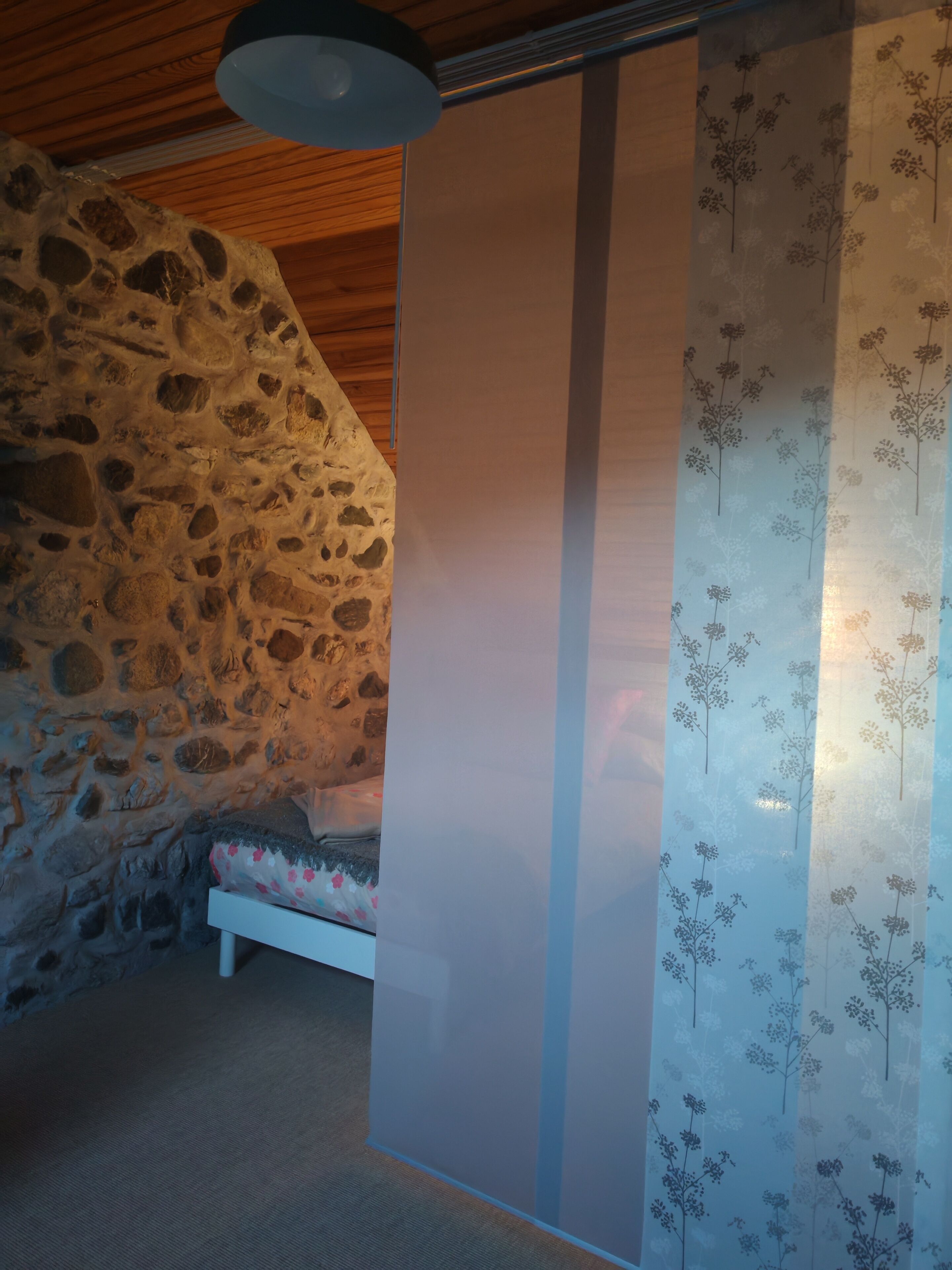 Ein Zimmer mit Steinwand, einem Bett mit floraler Bettwäsche und einem Vorhang mit Blumenmuster.