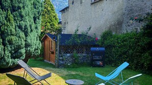 Ein Garten mit einem Holzschuppen, einem Grill und zwei Liegestühlen.