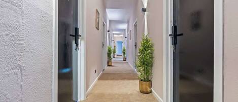 A hotel hallway with carpeted floors, doors with numbers, and potted plants.
