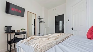 Ein Schlafzimmer mit Bett, Wandfernseher, Schreibtisch mit Stuhl und Kleiderständer.