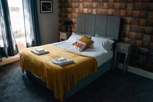 Una cama con cabecera, una mesita de noche, una lámpara y una ventana con cortinas.
