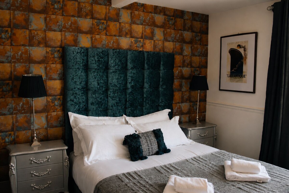 Una habitación de hotel con una cama grande, dos mesitas de noche, un cabecero y un cuadro enmarcado en la pared.