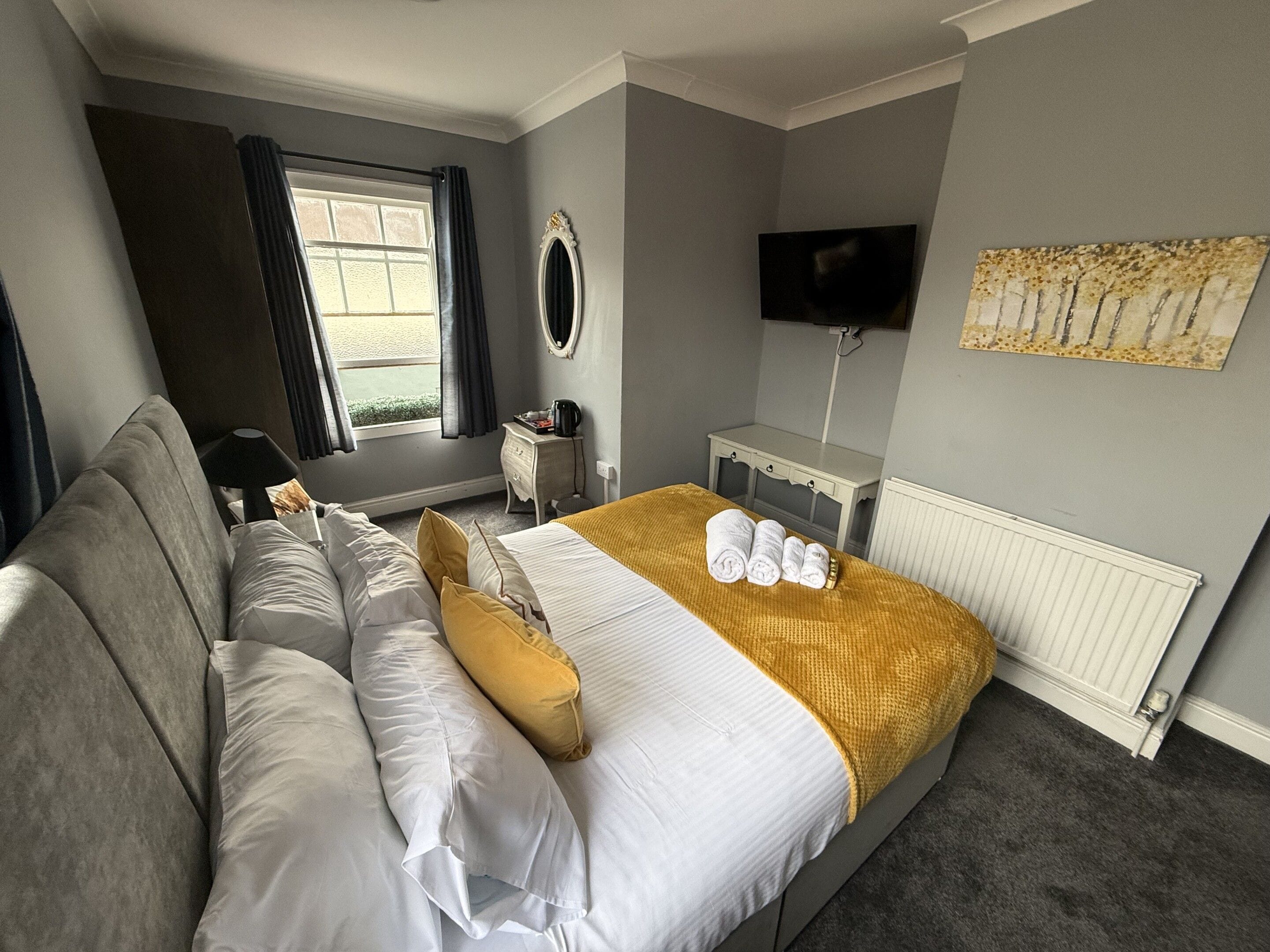 Habitación de hotel con cama, sofá, mesita de noche, televisión y ventana con cortinas.