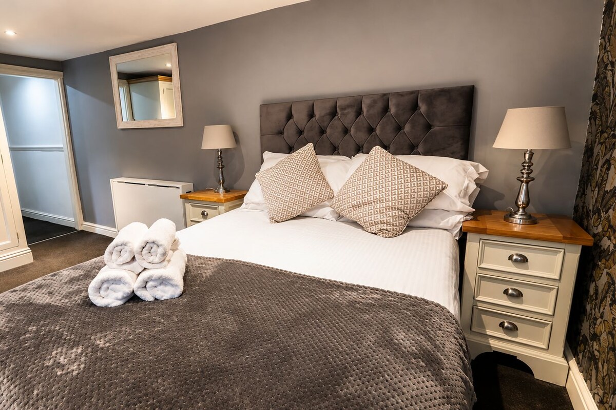 Una habitación de hotel con cama, dos mesitas de noche, un armario y un espejo.