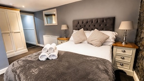Una habitación de hotel con cama, dos mesitas de noche, un armario y un espejo.