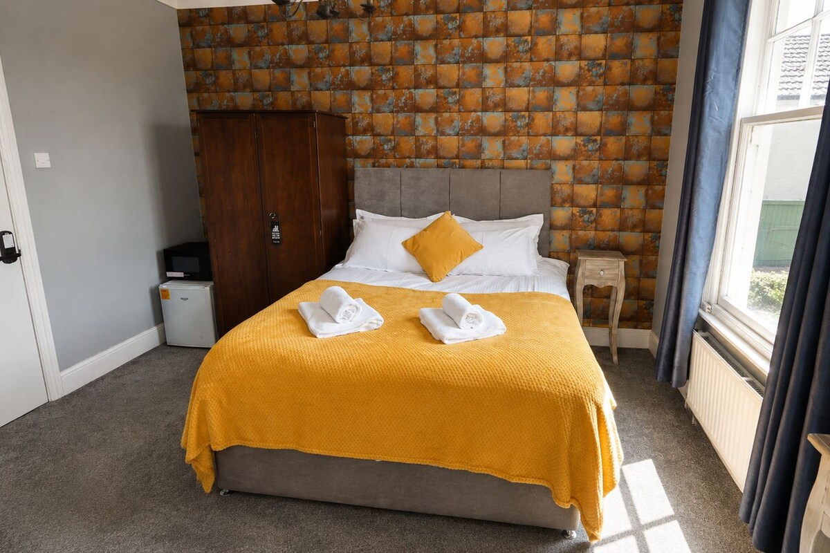 Una habitación de hotel con cama, armario, mesita de noche y ventana con cortinas.
