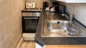 A compact kitchen with a built-in oven, a stovetop, a sink, and a microwave. - The Lobster Pots - Bawtry (Bawtry)