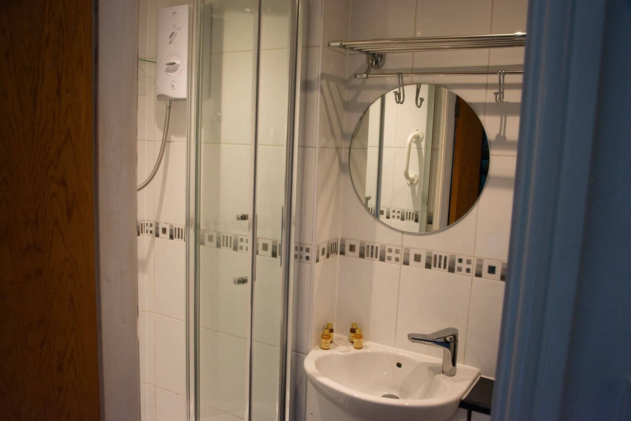 Ein modernes Badezimmer mit Duschkabine aus Glas, einem weißen Waschbecken und einem runden Spiegel.
