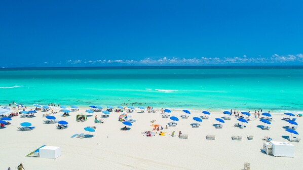 A beach with numerous sun loungers and umbrellas, a clear blue sky, and turquoise waters. - Private Residence at Carillon Resort - 910 (Miami Beach)